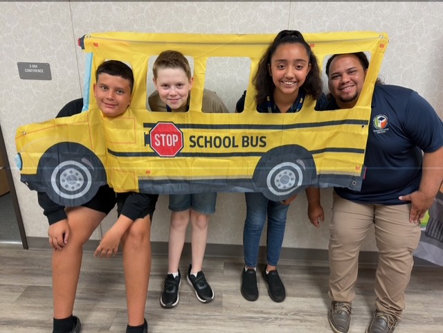 Kids and staff holding and looking out a school bus frame